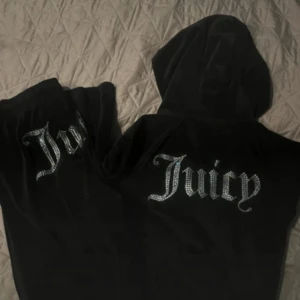 Svarta Juicy Couture mjukisbyxor - Svarta mjukisbyxor från Juicy Couture i glansig sammet med strassdetaljer och stor Juicy-logga på baksidan. Byxorna har en relaxed passform och resår i midjan för extra komfort. Perfekta för en chill och trendig look.