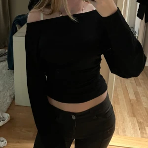 Svart offshoulder topp - Säljer en svart offshoulder topp med långa ärmar och croppad passform. Toppen har en stilren och enkel design som sitter snyggt över axlarna. Perfekt att styla med höga byxor för en trendig look.