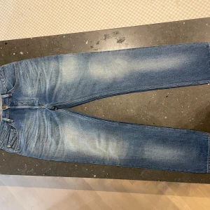 Blå jeans från Diesel straight fit - Snygga blå jeans från Diesel med klassisk femficksdesign och ljusa slitningar på låren och knäna. Modellen har raka ben och normal passform, med brunt läderpatch med Diesel-logga bak i midjan. Perfekta för en chill och stilren look.
