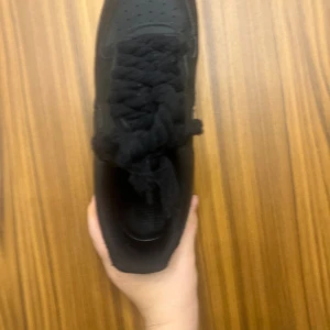 Nike Air Force 1 helsvarta sneakers - Säljer ett par helsvarta Nike Air Force 1 sneakers i storlek 45. Skorna har klassisk siluett, rund tå, platt sula och är tillverkade i skinn med grova svarta snören. Perfekta för dig som gillar en clean och tidlös look. KAN DISKUTERA PRIS
