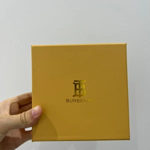 Brunt Burberry bälte med guldspänne - Säljer ett snyggt brunt bälte från Burberry med klassiskt randigt mönster och exklusivt guldspänne. Bältet kommer i originalförpackning med Burberry-kort och kvitto. Perfekt accessoar för att lyfta din outfit med en lyxig touch.