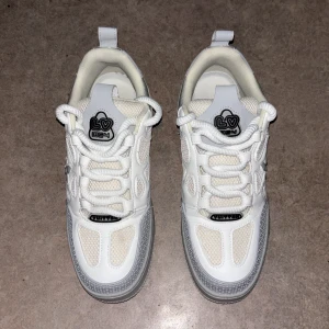 IV skates - Säljer ett par Trainer sneakers i vitt och ljusgrått med coola detaljer och grafiska tryck. Skorna har snörning, platt sula och meshpaneler för extra komfort. Ikonisk blomdetalj på sidan och broderad logga på hälen. Perfekt för dig som gillar exklusiv streetwear.