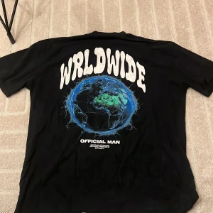 Svart Worldwide t-shirt från BoohooMAN - Svart t-shirt från BoohooMAN med stort tryck på ryggen: 'WRLDWIDE' och en blågrön jordglob. Texten 'OFFICIAL MAN' under motivet. Klassisk passform, rund hals och korta ärmar. Perfekt statement-plagg för dig som gillar streetwear.