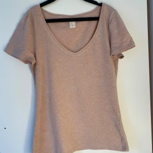 Ljusrosa v-ringad t-shirt från H&M - En basic ljusrosa t-shirt från H&M med v-ringning och korta ärmar. Tillverkad i mjuk bomull med lite stretch för en skön passform. Perfekt till jeans eller kjol för en enkel och clean look.
