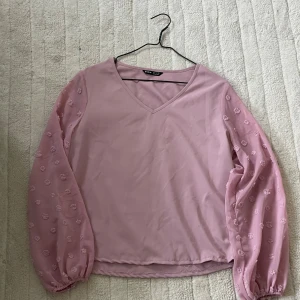Rosa blus - Säljer en ljusrosa blus från shein i storlek S. Blusen har v-ringad hals och transparenta långärmade ärmar med broderade prickar. Materialet känns lätt och flowy, perfekt för dig som gillar romantiska detaljer och mjuka färger. Säljer då den inte kommer till användning😊