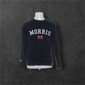 Mörkblå sweatshirt från Morris - Mörkblå sweatshirt från Morris med vit broderad logga och brittisk flagga på bröstet. Klassisk rund halsringning och långa ärmar. Perfekt för dig som gillar stilren och sportig look.