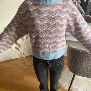 Pastellfärgad stickad tröja med zigzag - Superfin stickad tröja i pastelliga färger med zigzag-mönster i ljusblått, rosa, beige och vitt. Tröjan har ribbade muddar och nederkant, samt lång ärm och rund hals. Perfekt för dig som gillar färg och vill ha en mysig vibe.