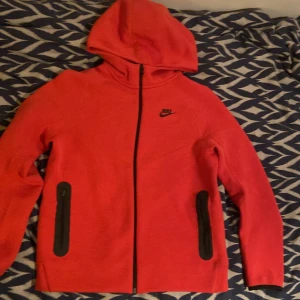 Röd Nike tech fleece XS - Nike hoodie i rött med svart logga på bröstet. Tröjan har hel dragkedja framtill, två svarta fickor med dragkedja och en skön huva. Perfekt för chill eller träning, i mjukt bomullsmaterial och långärmad modell. Den är använd max 1 gång så nyskick. Storlek XL 158-170 i barn men passar XS.