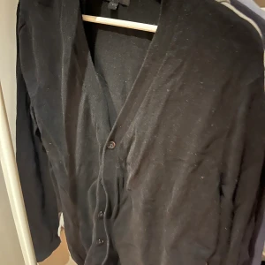 Svart kofta från ASOS i bomull - Svart kofta från ASOS i storlek S. Klassisk modell med v-ringning och knappar framtill. Långärmad och tillverkad i mjuk bomull, perfekt att slänga över en t-shirt eller skjorta. Enkel och stilren design som funkar till det mesta.