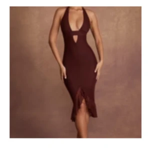 Brun halterneck långklänning med volang - Supersnygg brun långklänning med halterneck och djup v-ringning. Klänningen har en tight passform, rynkade detaljer framtill och volang nertill med slits. Materialet är stretchigt och känns mjukt mot huden. Perfekt för dig som vill sticka ut med en elegant och trendig look.