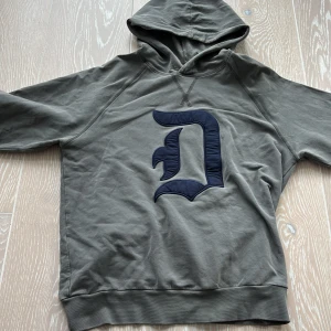 Grå hoodie från Dondup med blå D - Snygg grå hoodie från Dondup med stor blå D-applikation på bröstet. Perfekt för chill dagar. Klassisk och stilren design med en modern touch. 