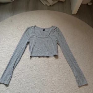 Grå croppad långärmad topp - Säljer en ljusgrå croppad topp med lång ärm och rundad urringning. Toppen är ribbad och har en slim passform som sitter snyggt på kroppen. Perfekt att styla med höga jeans eller kjol.