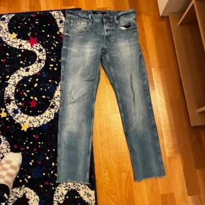 Replay ljusblå jeans, rak modell - Säljer ett par ljusblå jeans från Replay med snygg tvätt och råa, avklippta benslut. Klassisk femficksmodell med normal passform och raka ben. Jeansen är tillverkade i bomull och har Replay-logga på myntfickan.