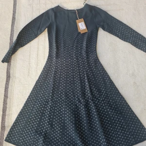 Mörkgrön långklänning från BOSS - Supersnygg långklänning från BOSS i mörkgrönt med diskret mönster över hela klänningen. Klänningen har lång ärm, rund halsringning och en lätt utställd kjol. Materialet känns mjukt och följsamt, perfekt till högtider.