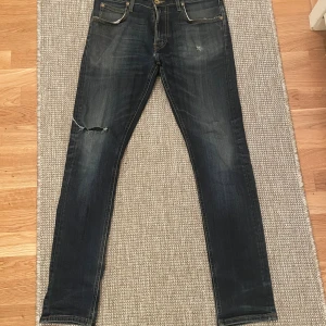 Mörkblå Lee jeans med slitning - Snygga mörkblå skinny jeans från Lee med slitningar och en trasig detalj på vänster knä. Klassisk femficksmodell med gylf och knapp, samt Lee-lapp bak i midjan. Jeansen har en smal passform och är tillverkade i stretchig denim för extra komfort.