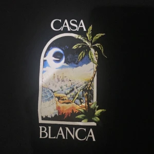 Svart sweatshirt från Casablanca - Svart sweatshirt från Casablanca med färgglatt tryck av stadsmotiv och palm på bröstet och ryggen. Tröjan har rund hals, långa ärmar och ribbade muddar. Perfekt för dig som vill sticka ut med en unik och snygg design.