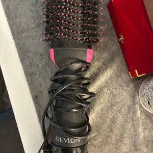 Revlon One-Step Hair Dryer & Volumizer - Revlon One-Step Hair Dryer & Volumizer i svart och rosa. Kombinerar hårtork och borste för enkel styling och volym. Synligt i gott skick, med mindre tecken på användning. Perfekt för att skapa slätt och fylligt hår snabbt hemma.