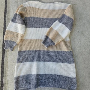 Randig stickad tröja i beige och grå - Mysig stickad tröja med breda ränder i beige, grått och vitt. Tröjan har lång ärm och ribbade muddar, perfekt för kyliga dagar. Oversized känsla och skön passform som funkar till jeans eller leggings.