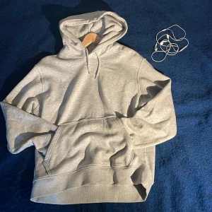 Grå hoodie från Weekday i bomull - Säljer en stilren ljusgrå hoodie från Weekday i mjuk bomullsmix. Klassisk modell med huva, snörning och stor magficka. Perfekt för chill dagar eller när du vill ha en enkel och clean look.