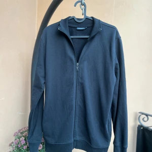 Svart ziptröja från Hanes - En svart långärmad ziptröja från Hanes med hög krage och ribbade muddar. Tröjan är i bomullsmaterial och har en enkel, clean look med dragkedja framtill. Perfekt för lager-på-lager och chill dagar. Storlek L sitter som M.