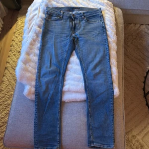 Nudie Lean Dean Lost Orange - Säljer ett par klassiska blå jeans från Nudie Jeans i storlek 32/32. Jeansen har fem fickor, orangea sömmar och raka ben med en snygg tvätt. Materialet är mjukt denim och passformen är normal med en modern look.