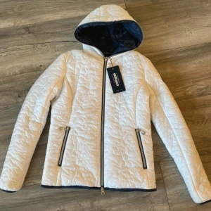 Vit jacka från Sebago - Snygg vit jacka från Sebago med mörkblått foder och huva. Jackan har dragkedja framtill, två fickor med dragkedja och en rund Sebago-logga på ärmen. Perfekt för dig som gillar stilren och sportig look. Storlek M men passar oxå S
