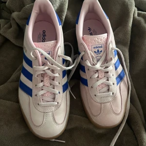 Adidas Gazelle rosa/blå sneakers - Säljer mina knappt använda Adidas gazelle, det är några defekter då jag haft byxor som färgat skon lite men annars används några fåtal gånger. Storlek 37 1/3 men passar mig bra som varierar mellan 36 och 37