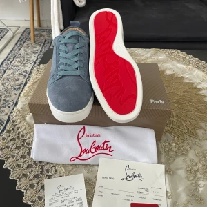  Christian Louboutin - Snygga blå sneakers från Christian Louboutin i mjuk mocka med klassisk röd sula och vita kanter. Skorna har rund tå, platt sula och matchande blå snörning. Insidan är i beige skinn med guldfärgad logga. Perfekta för dig som vill sticka ut med exklusiv stil.