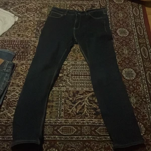 Crocker 322 Slim mörkblå jeans 32/32 - Mörkblå jeans från Crocker, modell 322 Slim. Klassisk femficksdesign med kontrastsömmar och läderpatch bak i midjan. Slim fit med raka ben och snygg passform. Perfekta för dig som gillar stilrena och tidlösa jeans.