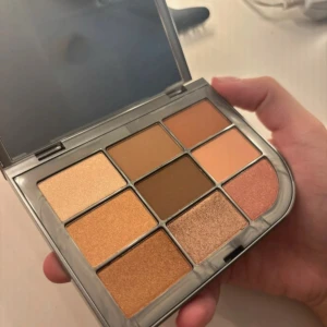 BeautyAct Bare To Go Eyeshadow Palette - Snygg ögonskuggspalett med nio nyanser i varma, neutrala toner. Paletten innehåller både matta och skimriga skuggor i brunt, beige, guld och koppar. Perfekt för att skapa allt från naturliga till mer markerade ögonlooks. Kommer i en stilren, grå plastförpackning med spegel.