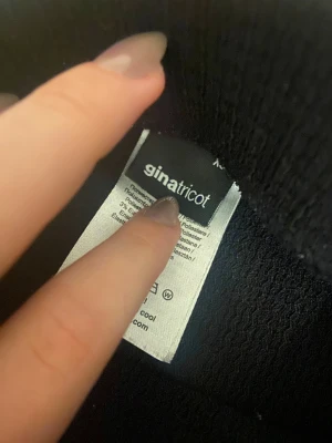 Svart omlottkjol med volang från Gina Tricot - Svart kort omlottkjol från Gina Tricot med snygga volangdetaljer längs kanten och knytband i midjan. Kjolen är gjord i mjukt polyestermaterial med lite stretch för skön passform. Perfekt för dig som gillar trendiga och feminina plagg.