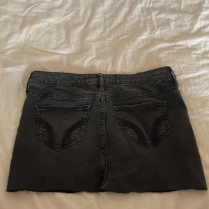 Hollister kjol - Säljer en svart jeanskjol från Hollister med rå kant nertill och klassiska femficksdetaljer. Kjolen har bälteshällor, knapp och dragkedja framtill samt bakfickor med snygga sömmar. Sytt den själv
