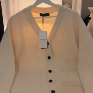 Beige kofta i ull från Zara - Helt ny med prislappen kvar! 699kr nypris. Säljer en beige kofta från zara i mjuk ullmix. Koftan har v-ringning, svarta knappar framtill och två fickor. Perfekt för lager-på-lager och chill stil. Passar dig som gillar klassiska och cleana plagg med lite oversized känsla. 