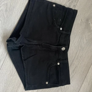 Svarta jeansshorts från H&M Divided - Säljer ett par svarta, tighta minishorts från H&M Divided. Klassisk femficksmodell med knapp och dragkedja framtill. Perfekta till sommaren och lätta att matcha med allt. Snygg och enkel design som alltid funkar. Passar även S.