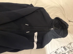 BOSS zip up svart - PRIS KAN DISKUTERAS! Svart hoodie från BOSS med vit logga på bröstet och vit rand på ena ärmen. Använd bara ett fåtal gånger.