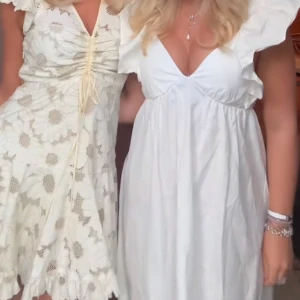 Vit kort studentklänning  - Supersöt vit kortklänning med djup v-ringning och stora volangärmar. Klänningen har en luftig passform och är tillverkad i ett lätt bomullstyg som ger en fräsch och somrig vibe. Perfekt för dig som gillar romantiska och trendiga detaljer.