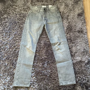 Grå jeans från Jack & Jones - Säljer ett par grå jeans från Jack & Jones, modell Relaxed/Chris. De har klassisk femficksdesign, raka ben och normal passform. Jeansen är tillverkade i slitstarkt denim och har bälteshällor samt knappstängning framtill. Storleken är W28 och L32. 