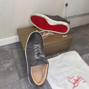 Grå mocka sneakers Christian Louboutin - Snygga grå sneakers från Christian Louboutin i mjuk mocka med klassisk röd sula och vita kanter. Skorna har rund tå, snörning och beige innersida. Perfekt för dig som vill ha en lyxig och stilren look, Använda fåtal gånger! Funkar föra både 42 och 43