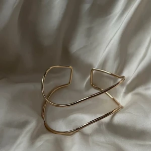 Guldigt minimalistiskt armband - Snyggt och stilrent armband i guldton med öppen design och mjuka, böjda linjer. Perfekt för dig som gillar enkel men modern stil. Armbandet är tunt och har en unik form som sticker ut på handleden. 14 k guldpläterad 💞 Justerbar 🩷