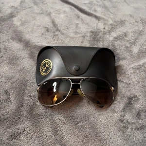 Ray ban solglasögon - Klassiska Ray-Ban aviator solglasögon med guldfärgad metallbåge och mörktonade glas. Säljs med original svart fodral med Ray-Ban-logga. Perfekt accessoar för en cool och tidlös stil.