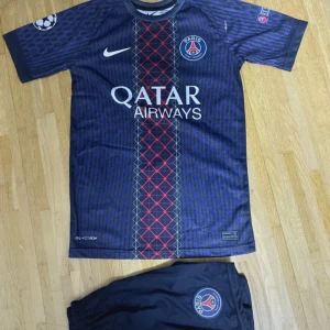 PSG Dembele matchtröja Nike blå - Säljer en officiell Paris Saint-Germain fotbollströja med O. Dembélé och nummer 10 på ryggen. Tröjan är marinblå med röda och grå detaljer, PSG-logga, Qatar Airways tryck och Champions League-märke på ärmen. Materialet är lätt och andas, perfekt för träning eller match.