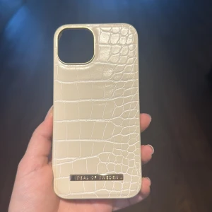 Ideal of Sweden iPhone Case Croco Cream - Elegant iPhone-skal från Ideal of Sweden i croco-mönstrad krämfärgad design. Skalet är i mycket fint skick utan synligt slitage och har en mjuk insida för extra skydd. Perfekt för dig som vill kombinera stil med funktion.