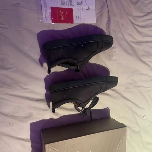Svarta sneakers från Christian Louboutin - Säljer ett par svarta sneakers från Christian Louboutin med klassisk röd sula och diskret logga. Skorna har rund tå, snörning och är tillverkade i mocka med en platt sula. Perfekt för dig som gillar exklusiv streetstyle och vill sticka ut med detaljer. Skorna e 2 månader gamla men finns några enstaka märken!