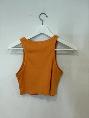 Orange ribbad croppad linnetopp - Säljer en orange croppad linnetopp från H&M. Toppen är ribbad och har breda axelband samt rund halsringning. Perfekt för varma dagar och enkel att styla med jeans eller kjol.