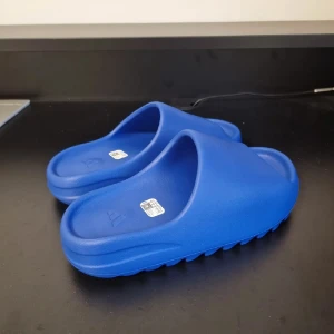 Blå Adidas slides sandaler - Säljer ett par blá Adidas slides med chunky, räfflad sula och öppen ta. Tillverkade i syntetmaterial för en lätt och bekväm känsla. Perfekta för sommaren och chill dagar. Adidas-logga pa fotbädden ger en clean och sportig vibe.