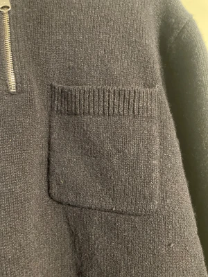 Svart stickad half zip-tröja, ARKET - Mysig svart stickad tröja med half zip och krage. Tröjan har en ribbad bröstficka på vänster sida och ribbade muddar vid ärmslut och nederkant. Perfekt för kyliga dagar och har en klassisk, enkel look som funkar till det mesta.