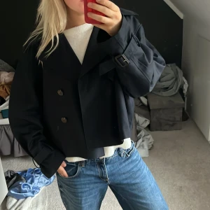 Mörkblå croppad rock från H&M - Snygg mörkblå croppad rock från H&M med dubbelknäppning och bred krage. Jackan har stora knappar, justerbara spännen vid ärmsluten och en loose fit. Perfekt för dig som gillar en stilren och trendig look.