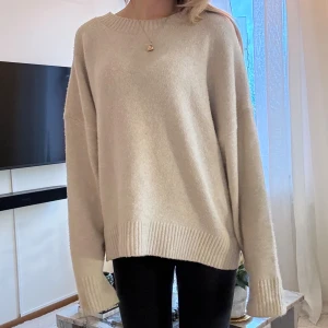 Beige oversized stickad tröja - Supermysig beige stickad tröja med oversized passform och långa ärmar. Tröjan har breda ribbade muddar vid ärmslut och nederkant samt rund halsringning. Perfekt för chill dagar och när du vill ha något extra comfy.