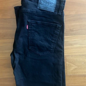 Svarta Levi's 505 jeans W31 L32 - Svarta Levi's 505 jeans med klassisk femficksdesign och rakt snitt. Jeansen har en diskret röd Levi's-tag på bakfickan och är tillverkade i slitstarkt denim. Perfekta för dig som gillar en tidlös och clean look.