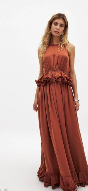 Rostbrun långklänning med volanger - Säljer en elegant rostbrun långklänning med volangdetaljer vid midjan och nederkanten. Klänningen är ärmlös och har en hög halsringning. ALDRIG ANVÄND